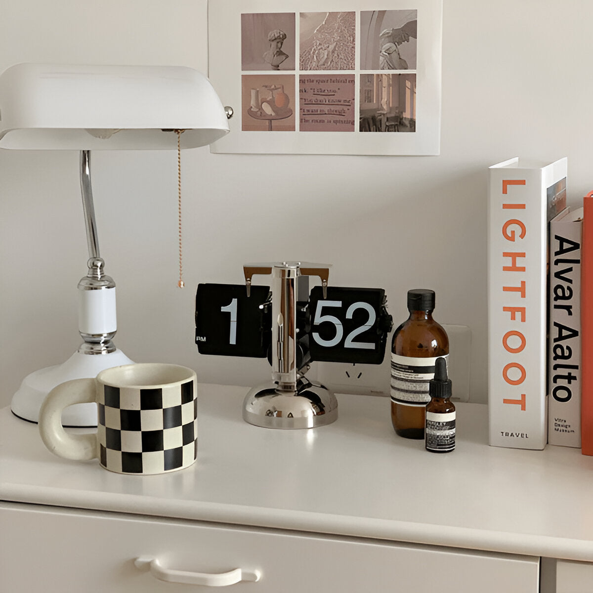 Desk with a lamp, checkered mug, digital clock, and books in a home office setting.