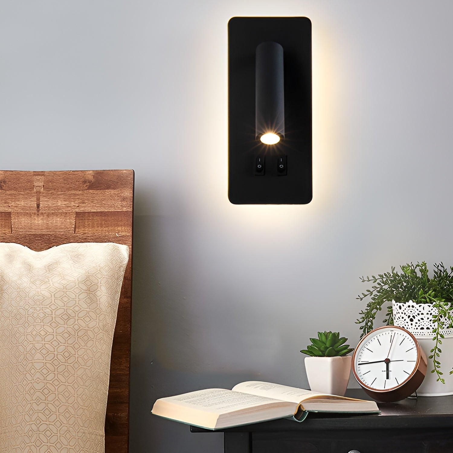 Modern wall sconce light fixture on a gray wall above a wooden headboard with a book and clock.