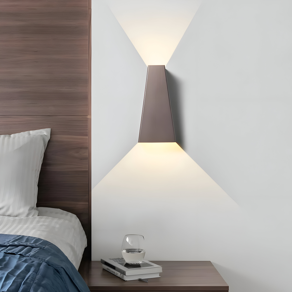 Modern wall lamp on a white wall above a wooden nightstand with books and a glass.