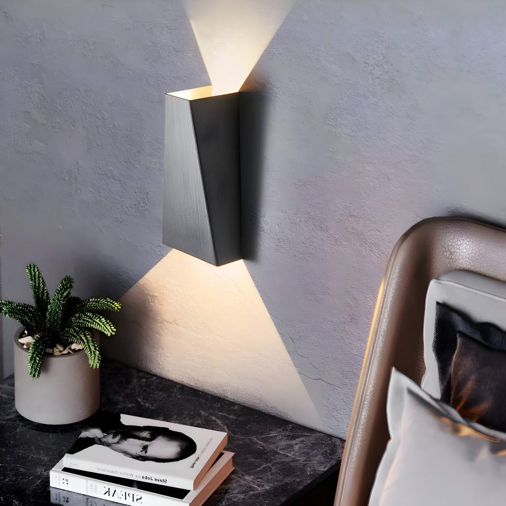 Modern wall lamp on a gray wall with a plant and books on a table.