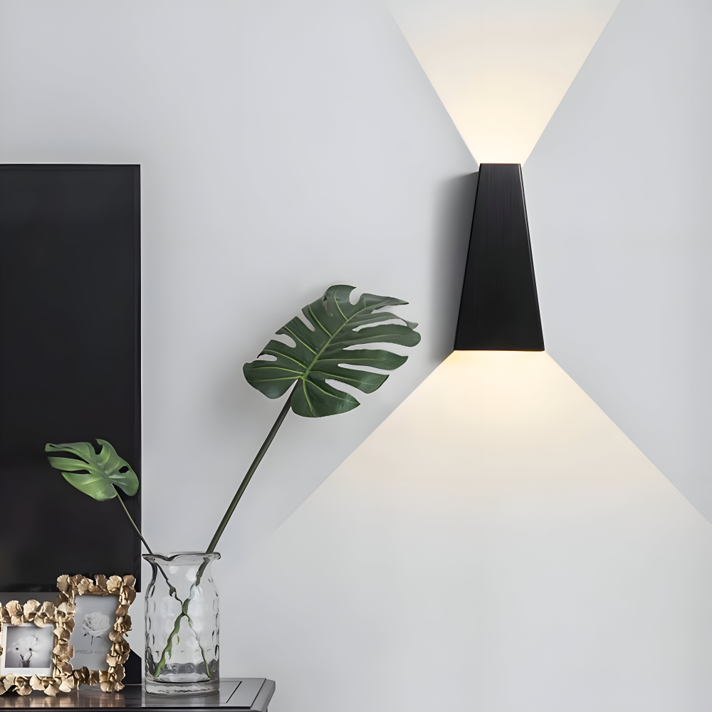 Modern wall lamp with a black shade on a white wall, next to a vase with a plant and decorative items.