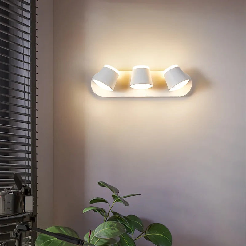 Modern wall-mounted light fixture with three white lamps on a neutral wall.