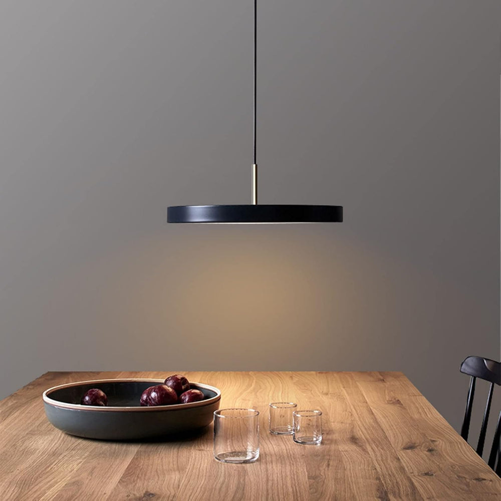 Black pendant light over a wooden table with a bowl and glasses on a gray wall background