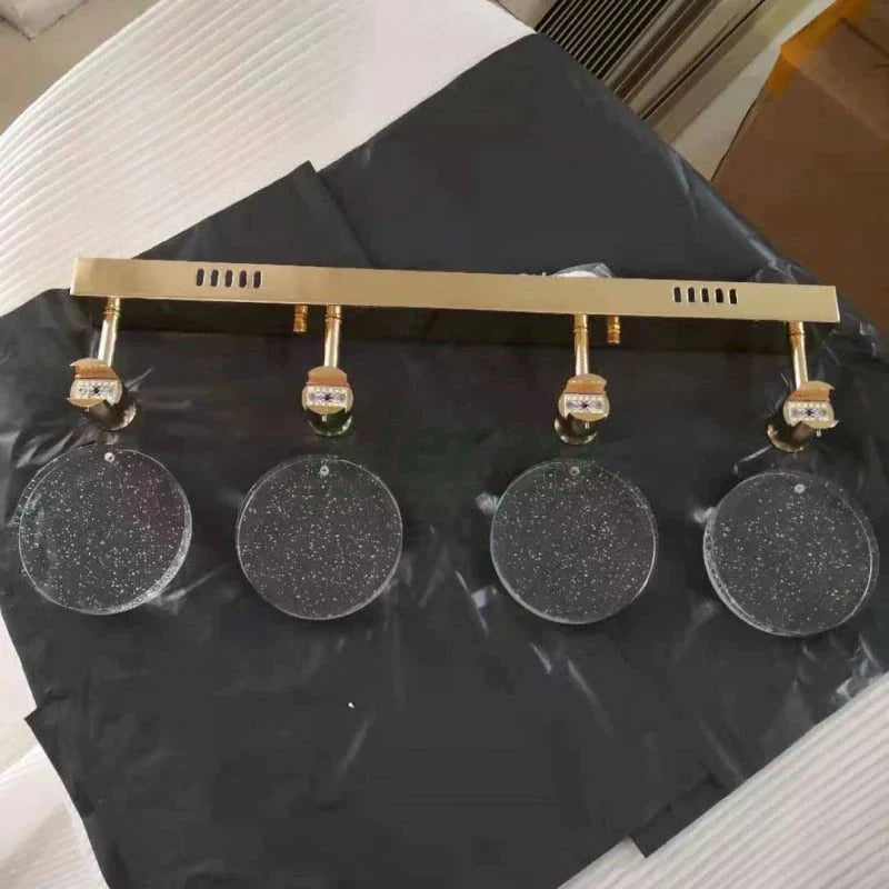 Gold-framed wall lamp display with four round, glittery earrings on a black surface.