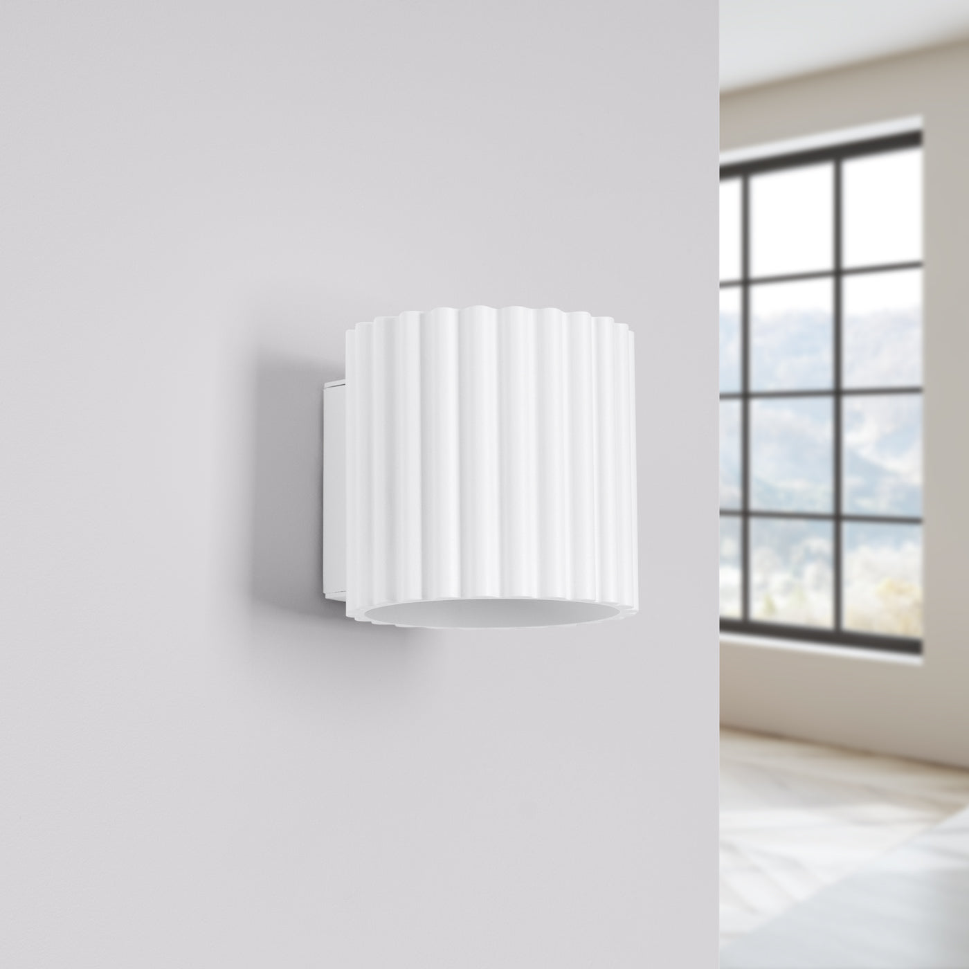 White wall-mounted lamp on a light gray wall with a window in the background