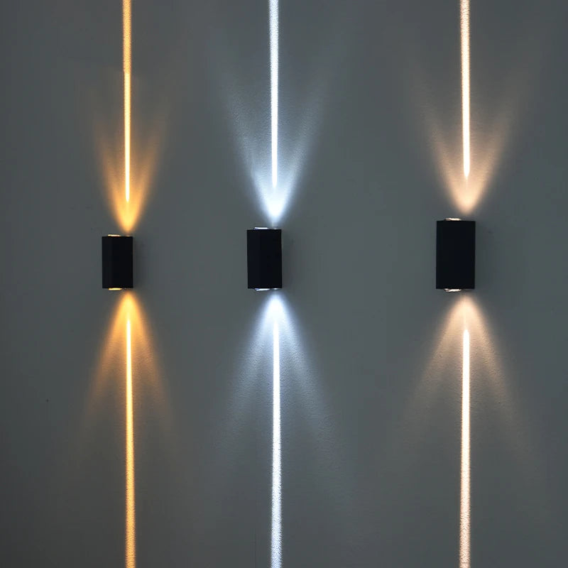Three wall-mounted lights casting different colored beams on a gray wall.
