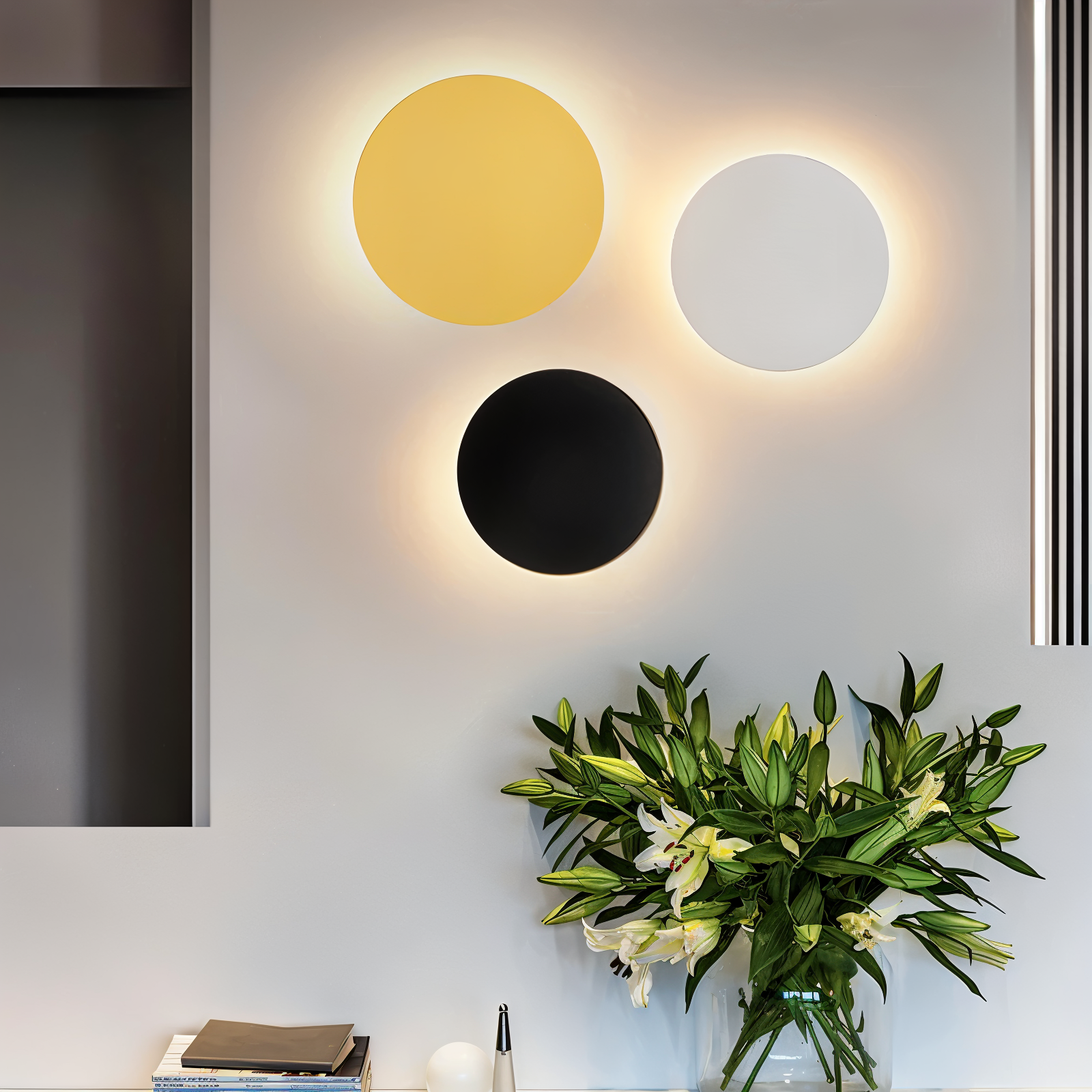 Three circular wall lights in yellow, black, and white above a vase with flowers on a table.