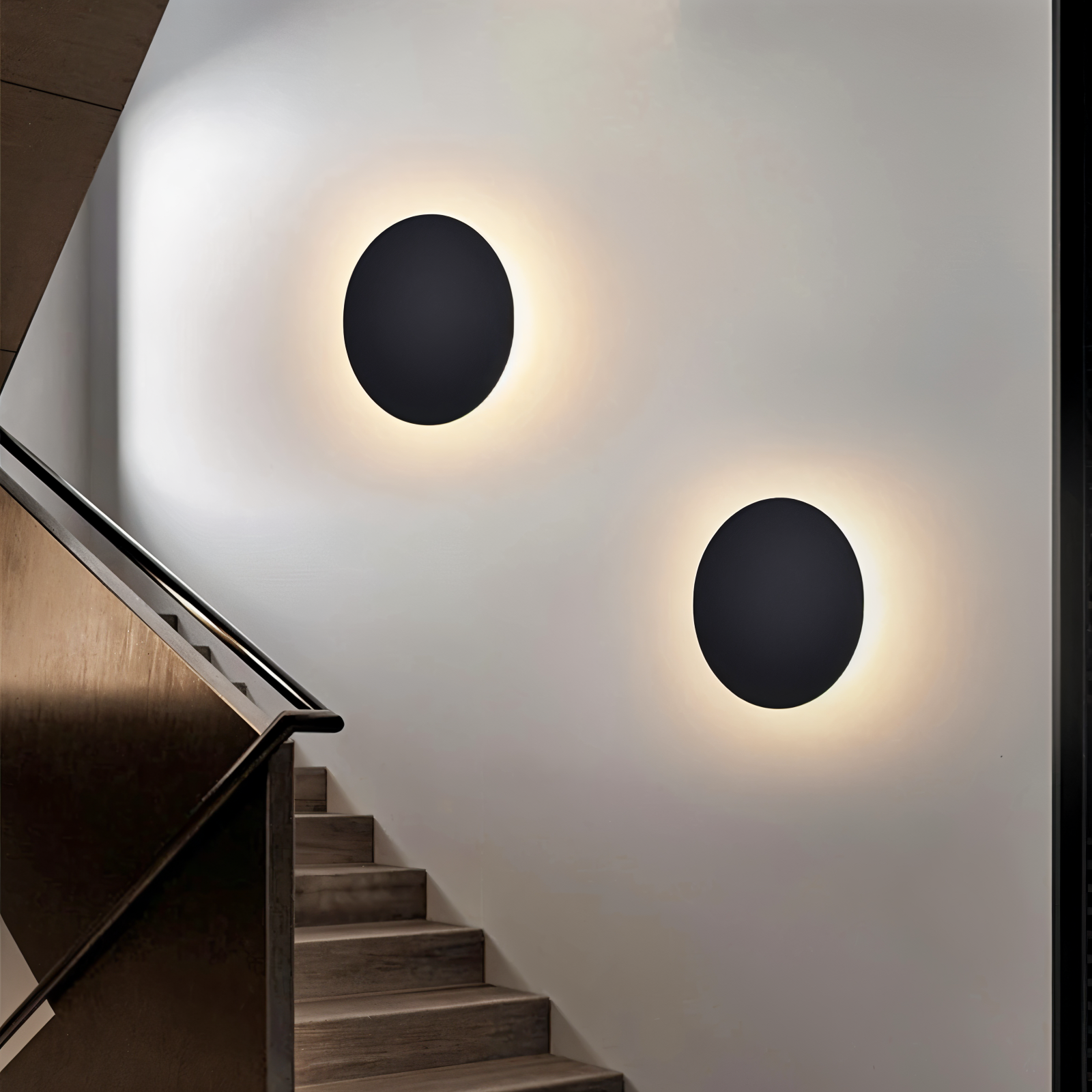 Two round black wall lights on a white wall with a staircase in the foreground.