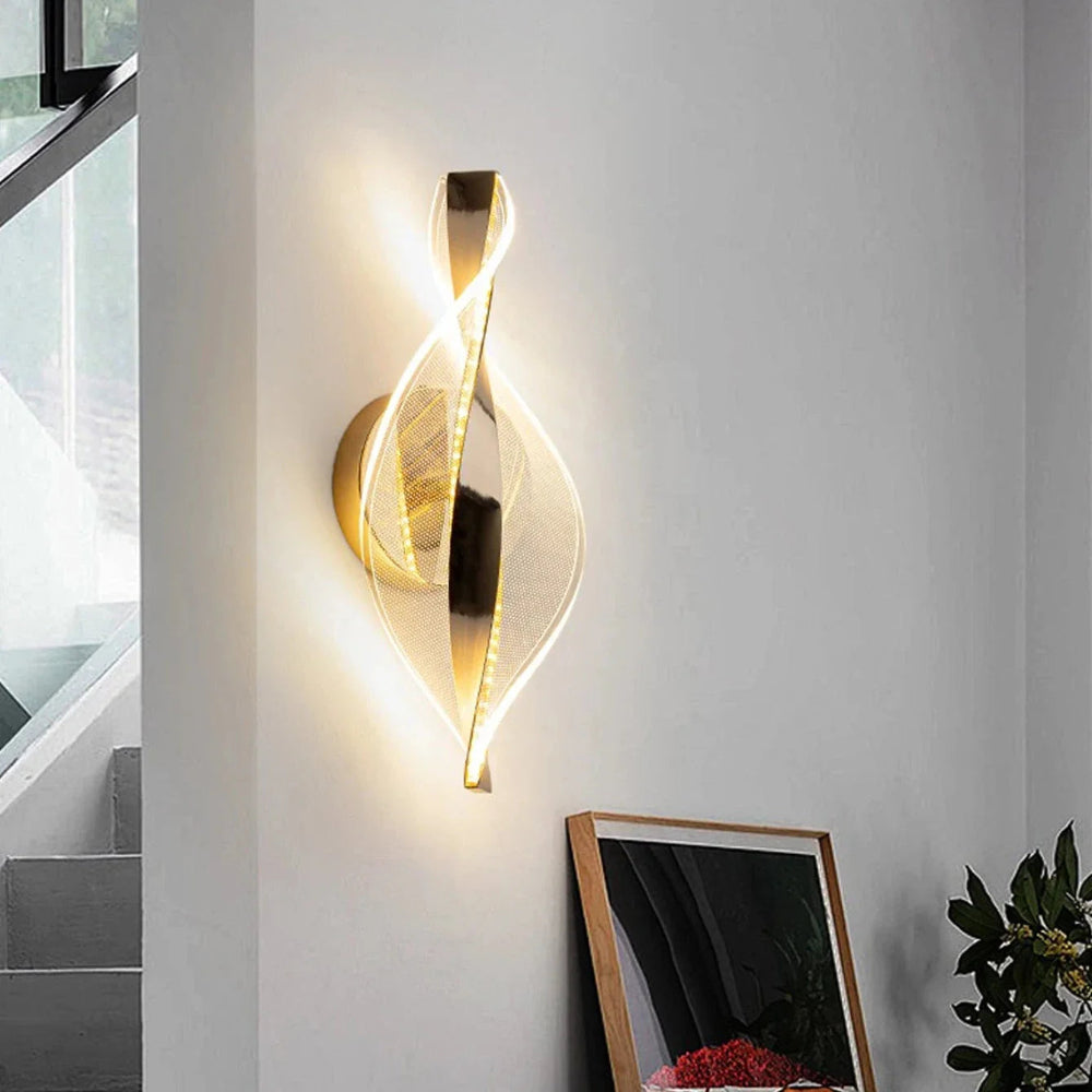 Modern wall sconce with gold finish on a white wall, staircase in the background