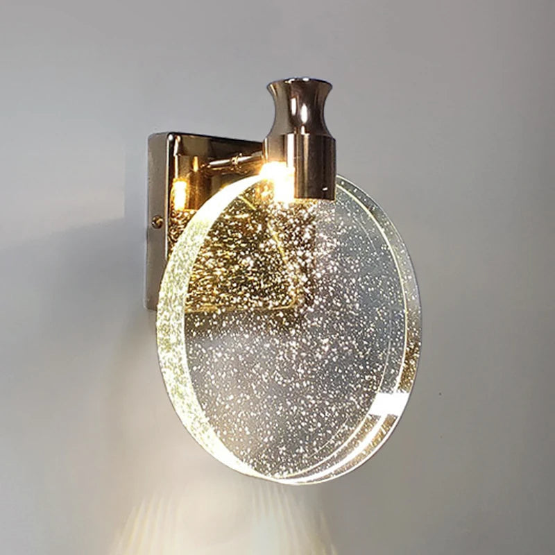 Wall-mounted light fixture with gold finish and clear glass shade on a gray background