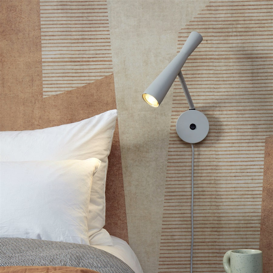 Wall-mounted lamp on a textured wall next to a bed with pillows