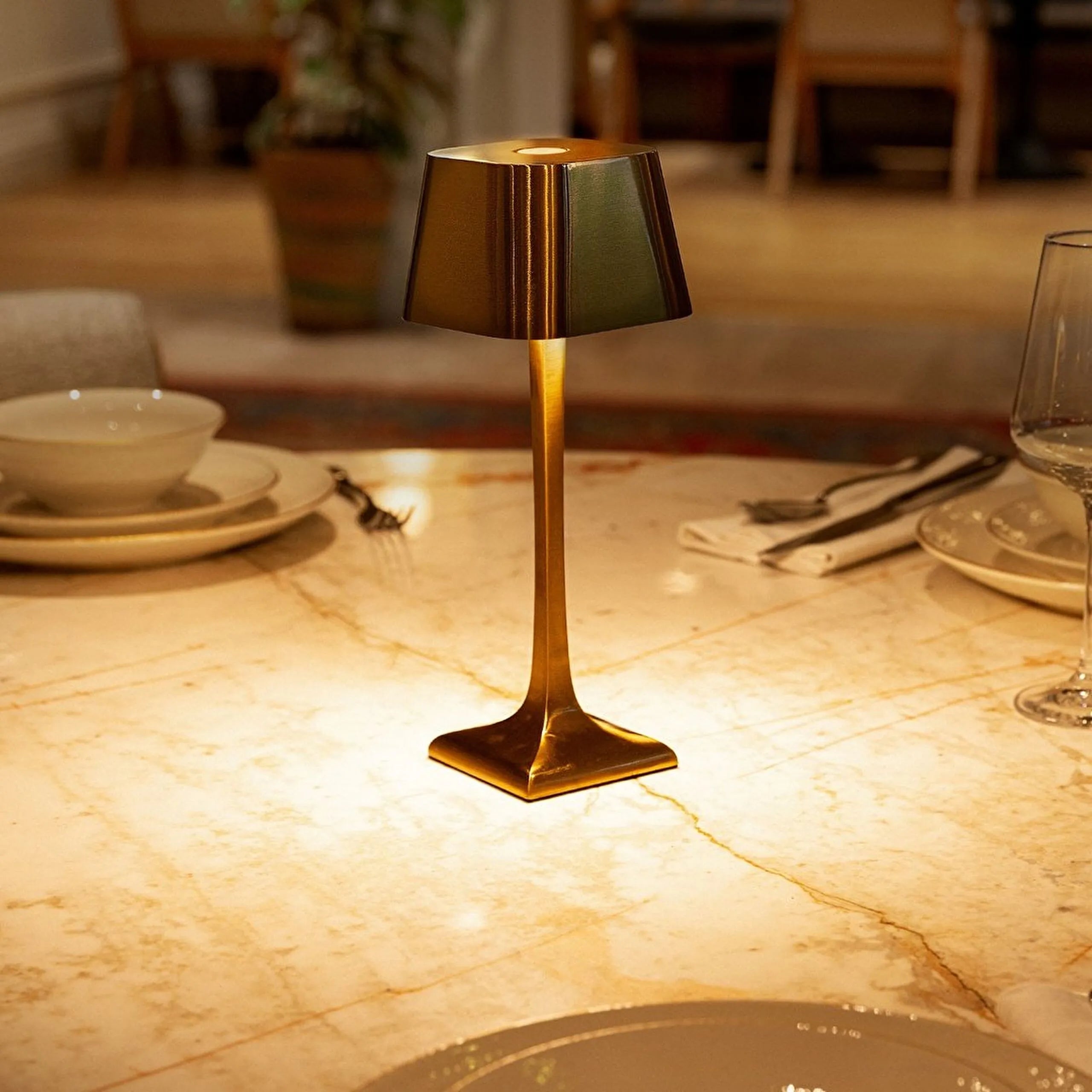 Gold table lamp on a marble surface with dining setup in the background