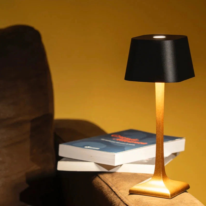 Black table lamp with gold base on a stack of books against a yellow wall.