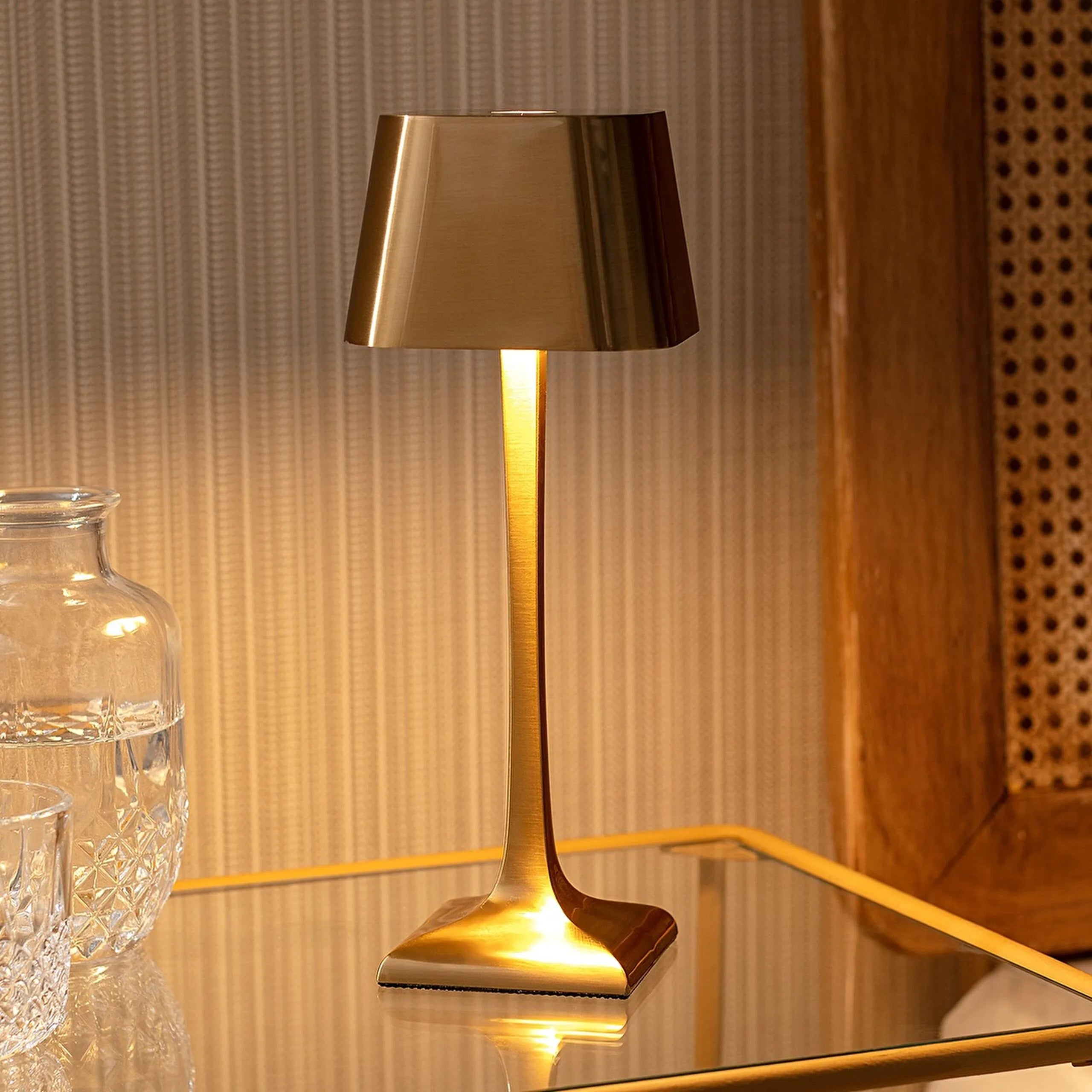 Gold table lamp on a reflective surface with a textured wall background