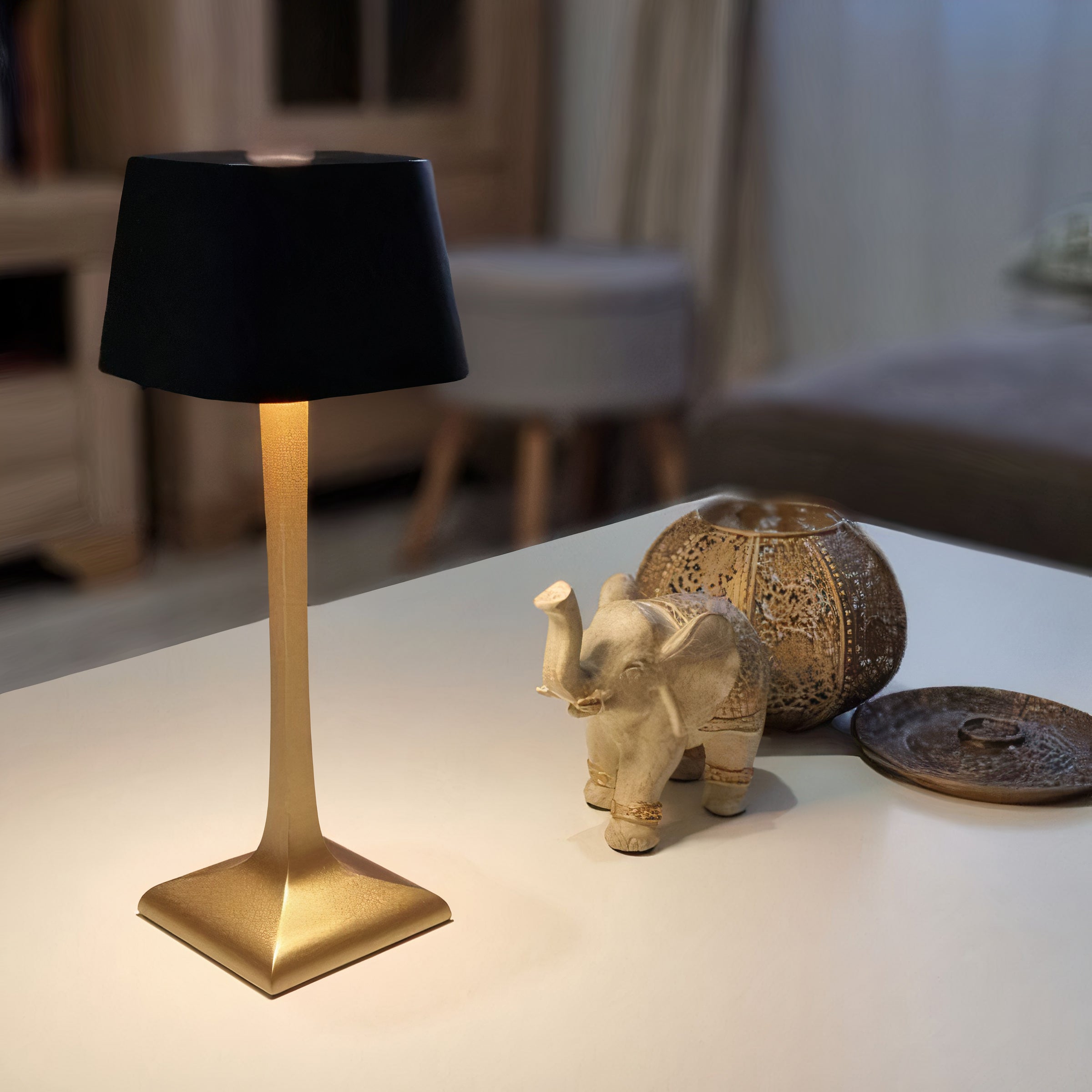 Decorative table lamp with a black shade and gold base on a surface with a blurred background.