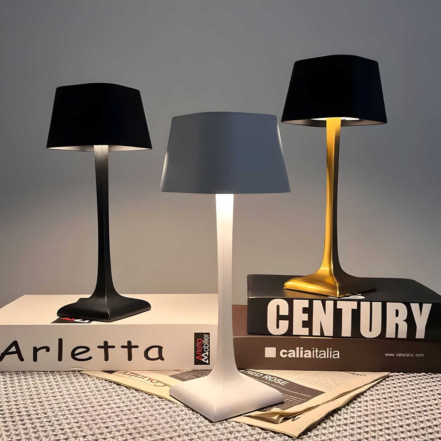 Three table lamps with different designs on top of books titled 'Arletta' and 'Century'.