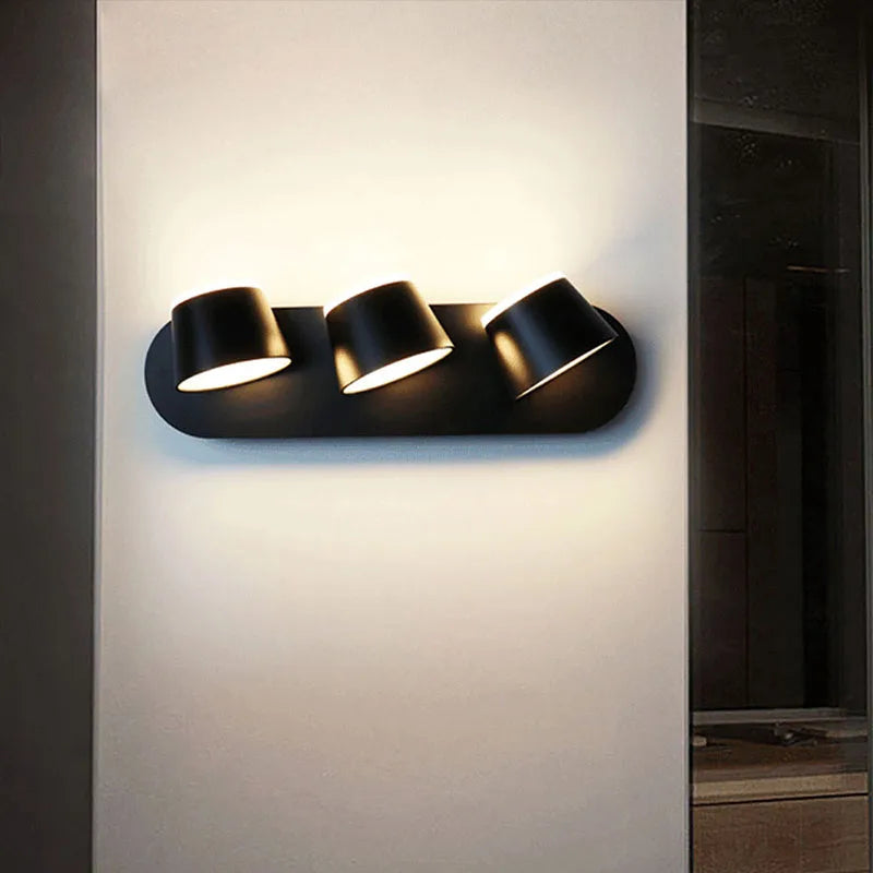 Modern wall-mounted light fixture with three cylindrical lights on a neutral wall.