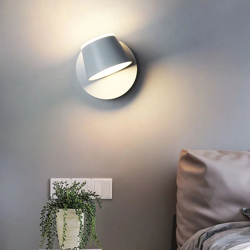 Modern wall light fixture on a neutral wall with a plant and bed in the background
