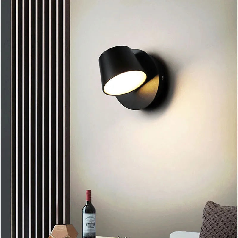 Black wall lamp on a light gray wall with a bottle of wine and decorative elements below.