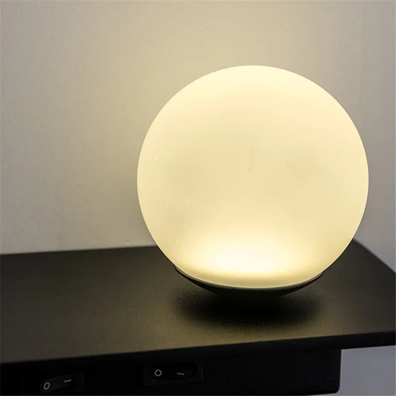 Spherical lamp emitting a warm glow on a dark surface with a neutral background