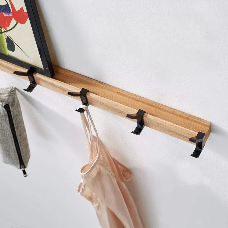 Wooden wall rack with black hooks holding a dress and a bag against a white wall.