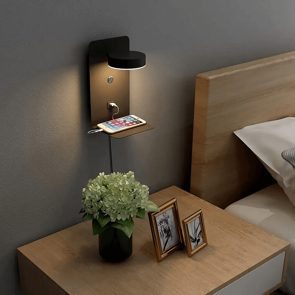 Wall-mounted lamp on a nightstand with a vase of flowers and photo frames.
