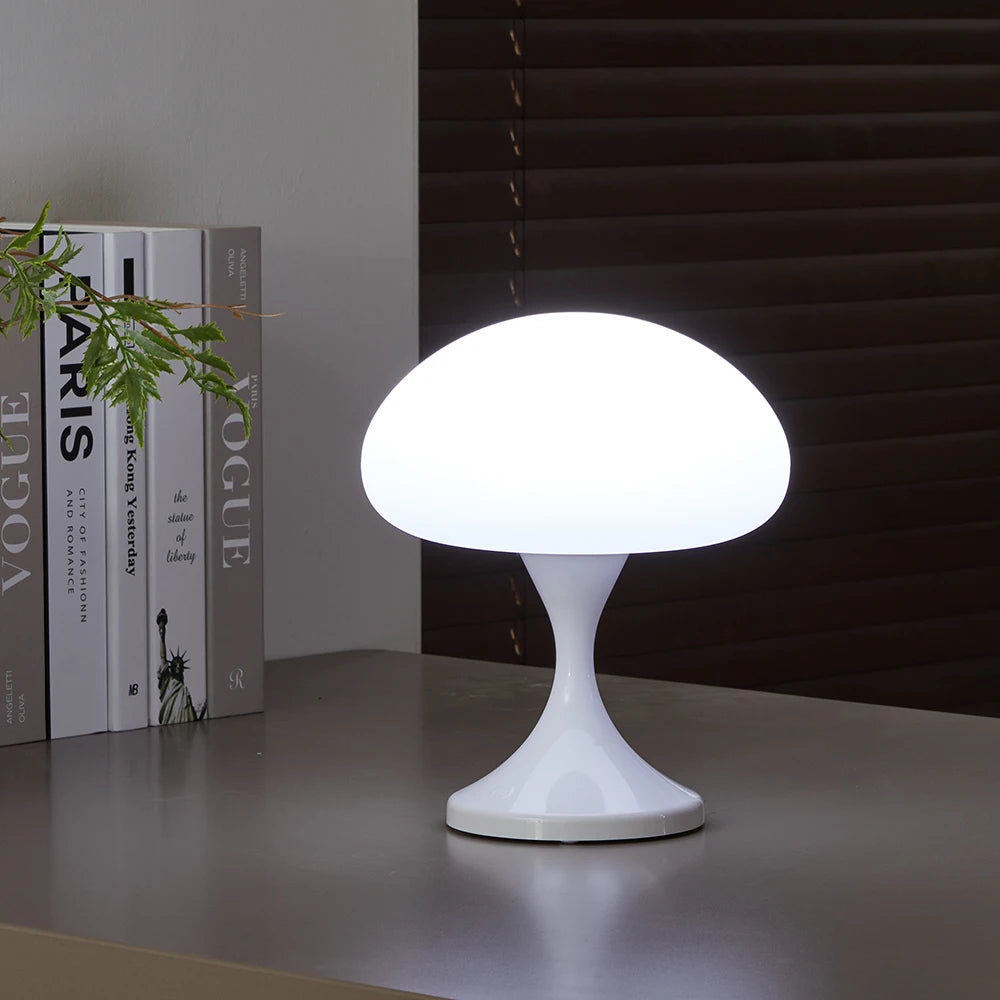White mushroom-shaped table lamp on a surface with books and a plant in the background