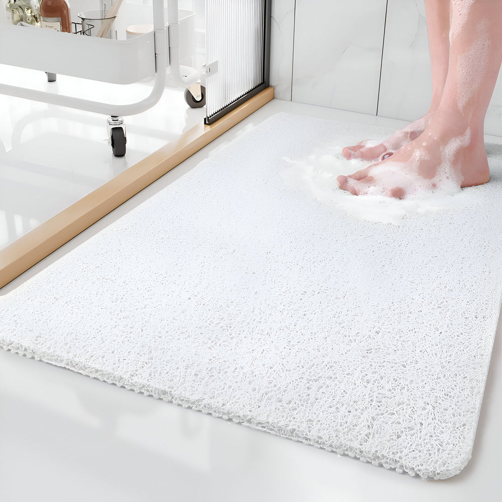 White bath mat on a bathroom floor with soapy feet stepping onto it.