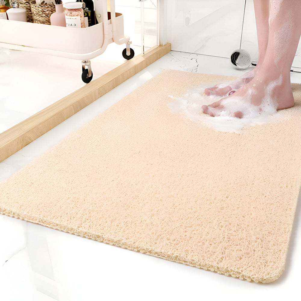 Beige bath mat on a bathroom floor with soapy feet stepping onto it.