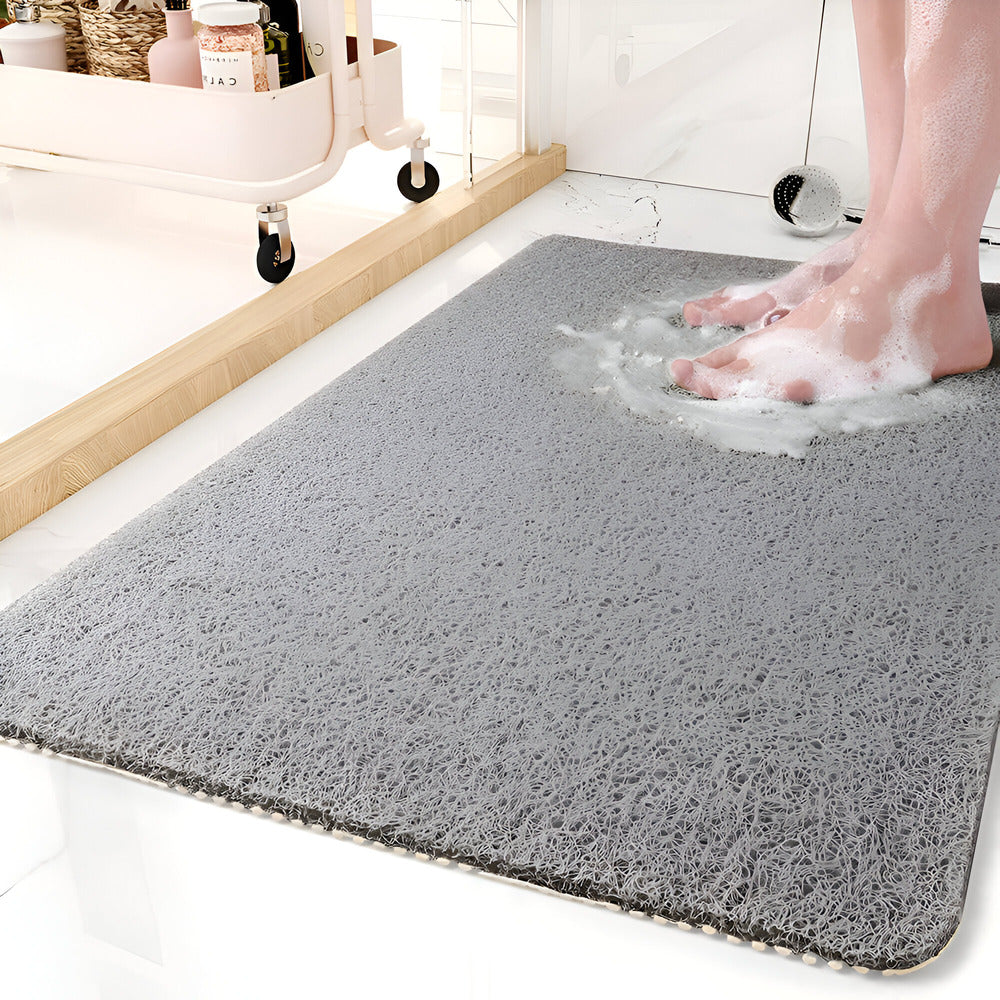 Gray bath mat with soapy water and feet stepping onto it in a bathroom setting.