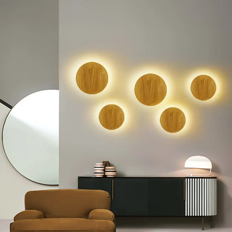 Modern wall lights with circular designs on a neutral wall, with a chair and cabinet in the foreground.