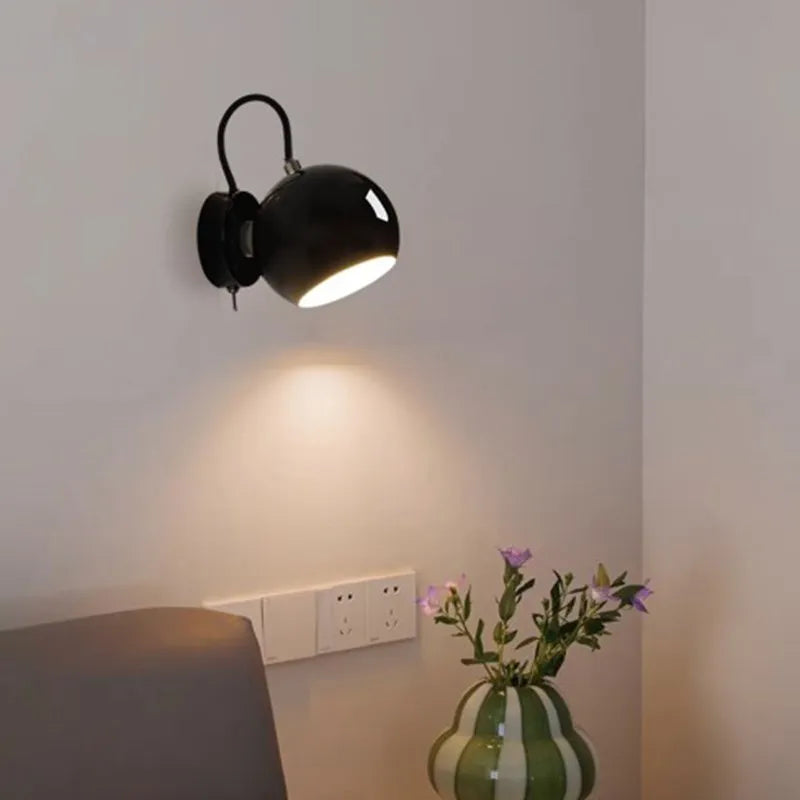 Black wall-mounted light fixture on a white wall with a vase of flowers in the foreground.