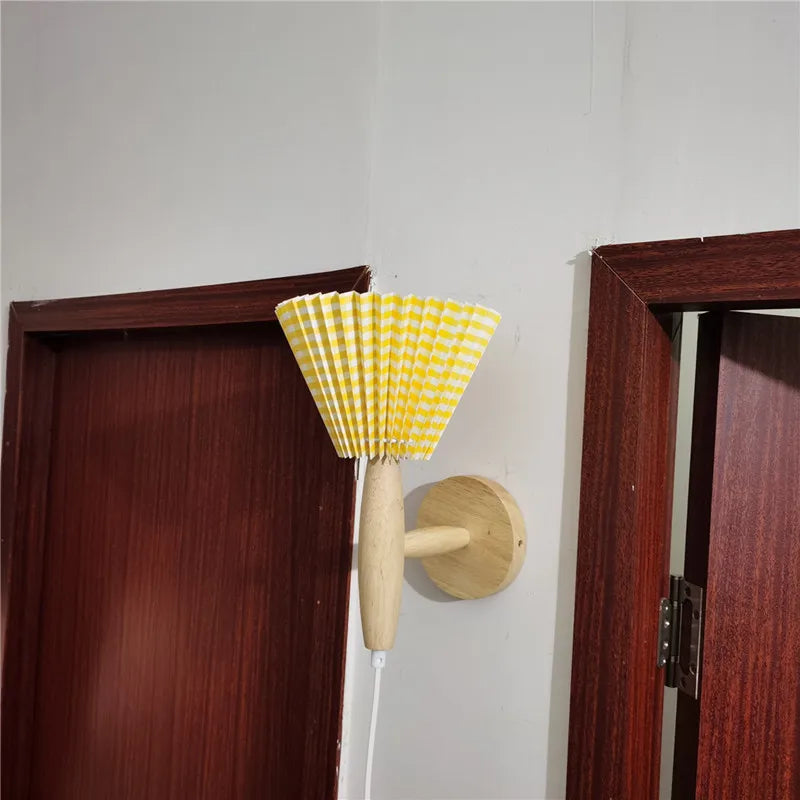 Yellow and white checkered lamp with wooden handle attached to a wall next to a door.