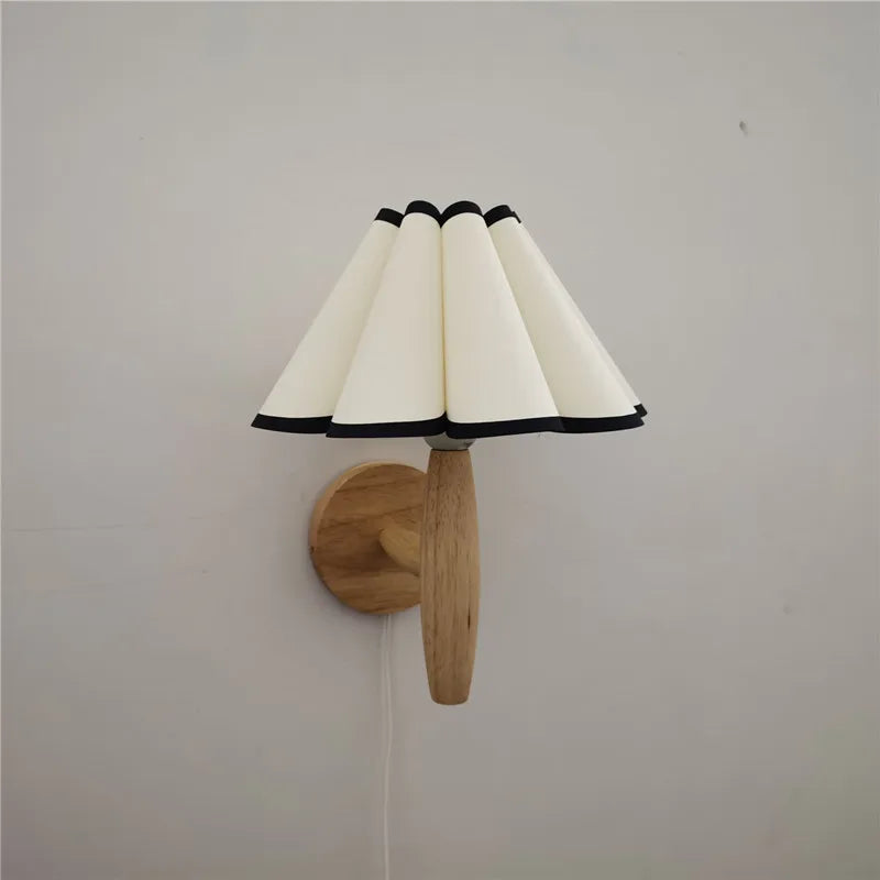 Wall-mounted lamp with a white shade and wooden base on a plain wall.