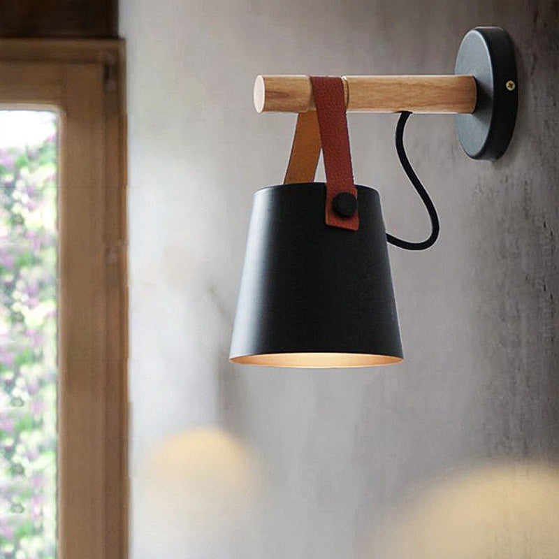 Wall-mounted lamp with black shade, wooden handle, and leather strap on a gray wall.