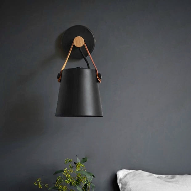 Black wall-mounted lamp with leather strap against a dark gray wall.