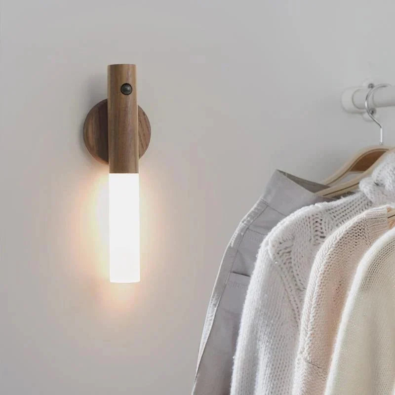 Wall-mounted light fixture casting a warm glow on a clothing rack with garments.