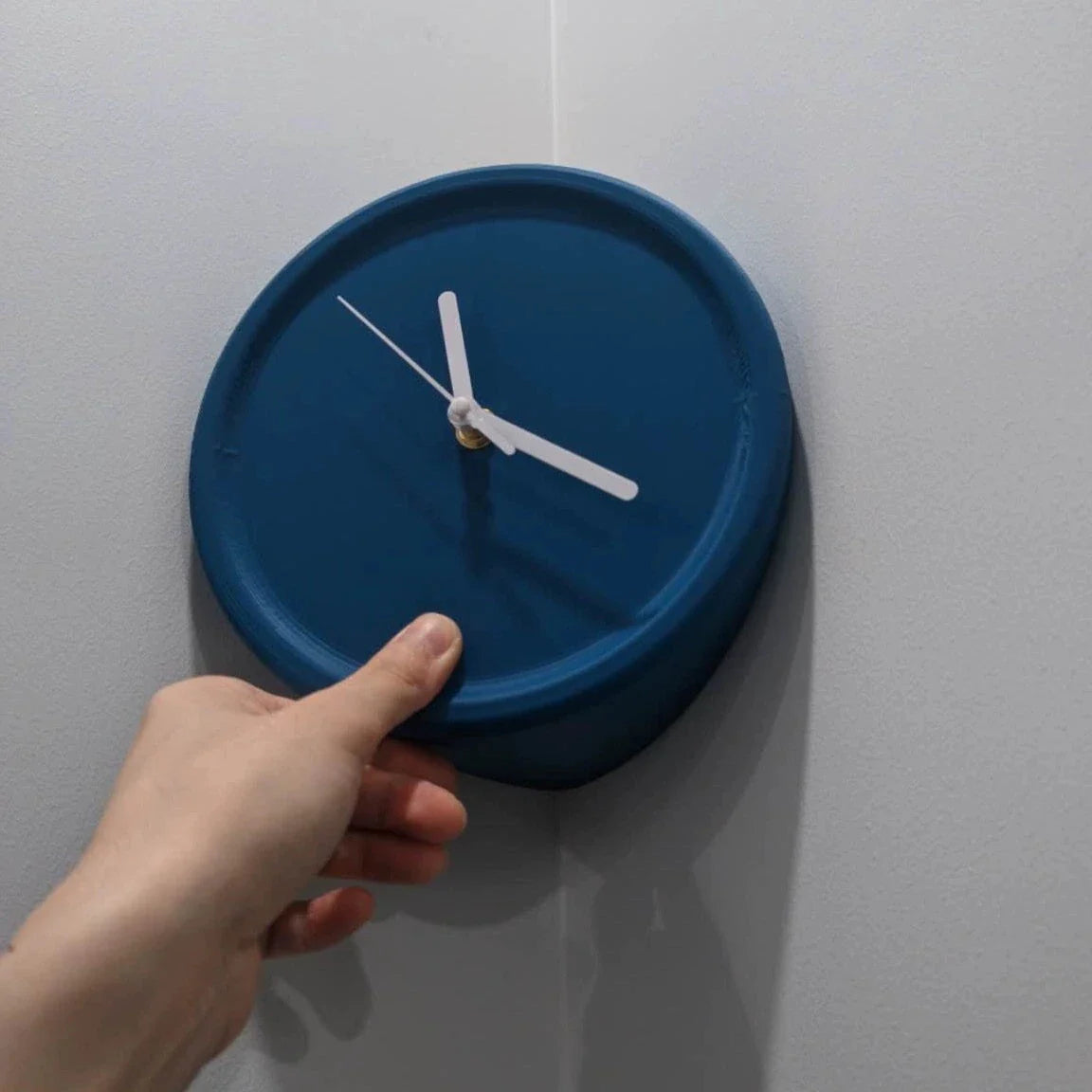Hand adjusting a blue wall clock against a white wall