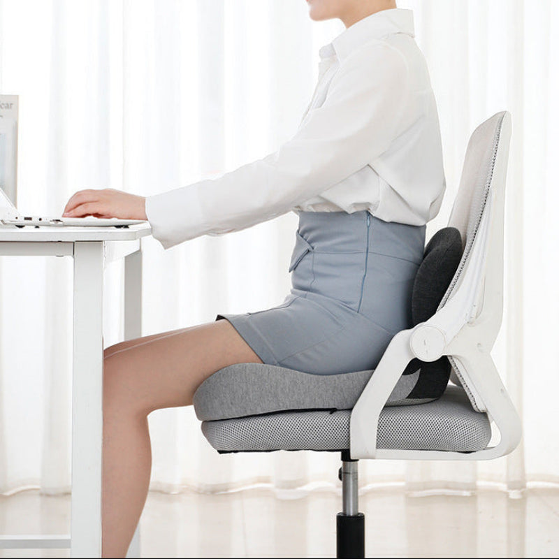 Person using a gray office chair with a cushion, sitting at a desk.