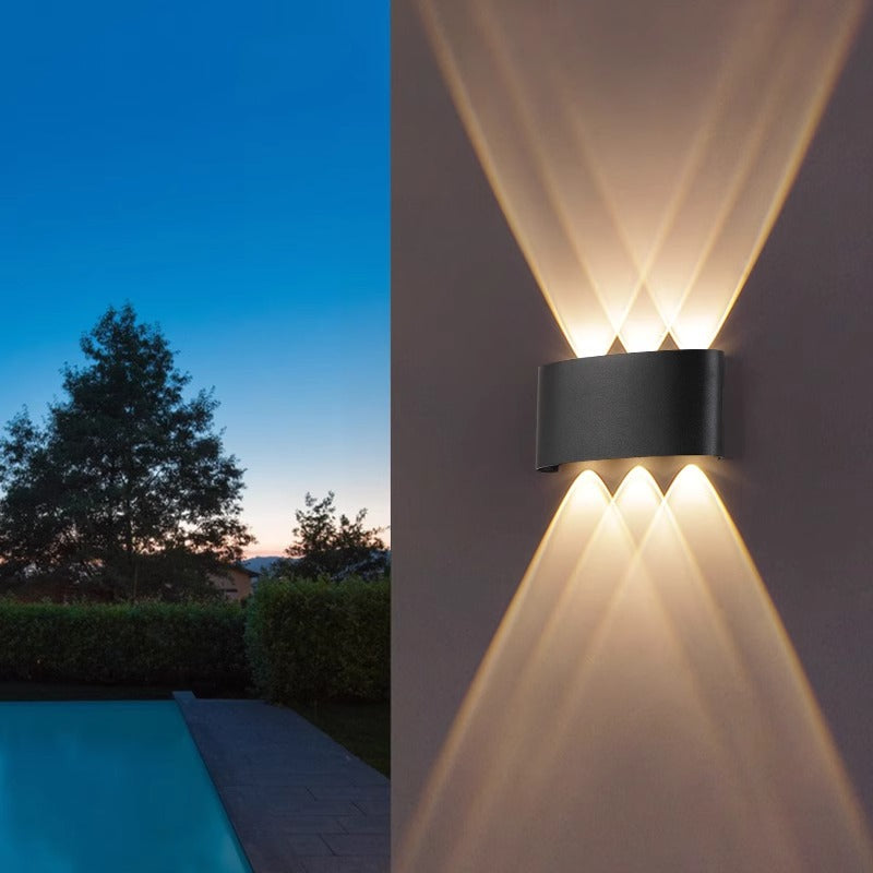 Outdoor wall light fixture on a building with a garden and pool in the background