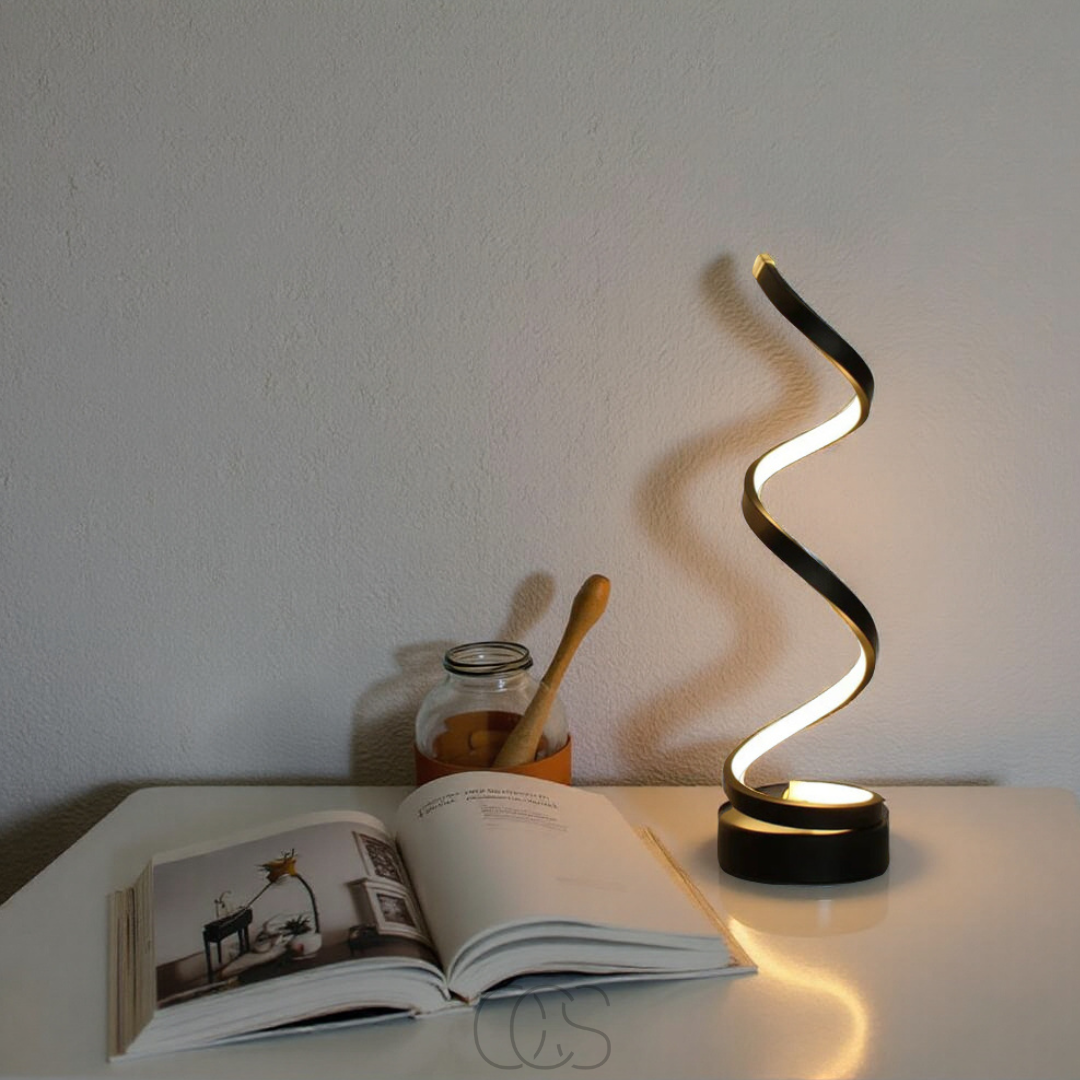 Spiral lamp on a table with an open book and jar in the background