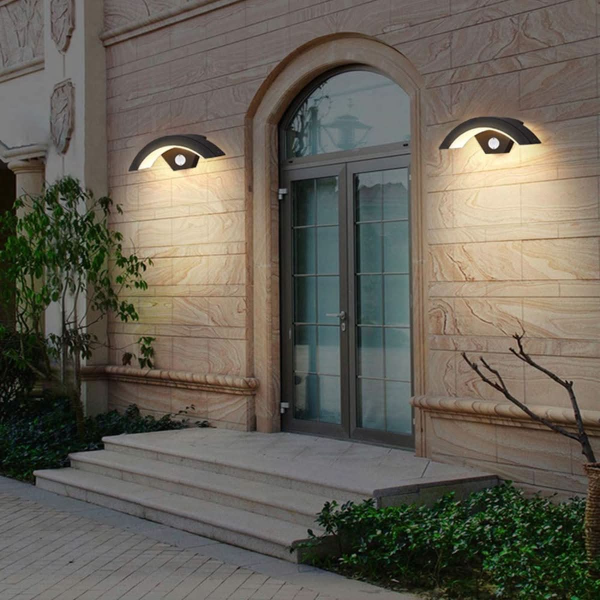 Elegant entrance with arched door and wall-mounted lights on a stone building.