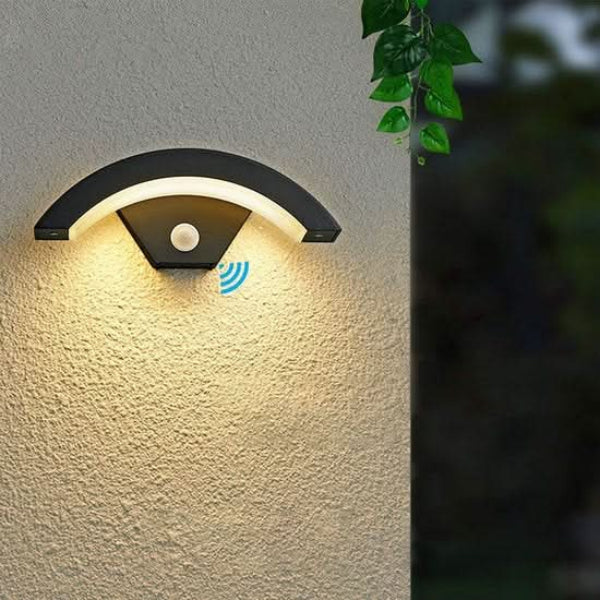 Outdoor wall light fixture on a textured wall with a blurred green plant in the background