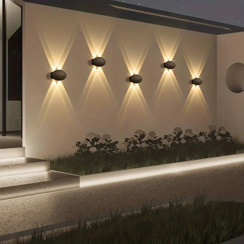 Modern outdoor wall lights on a textured wall with plants below.