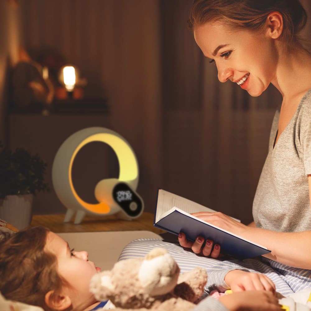 Woman reading a book to a child in a cozy room with a nightlight in the background.