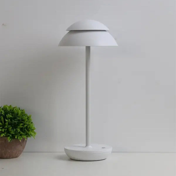 White table lamp on a white surface with a small plant to the left.