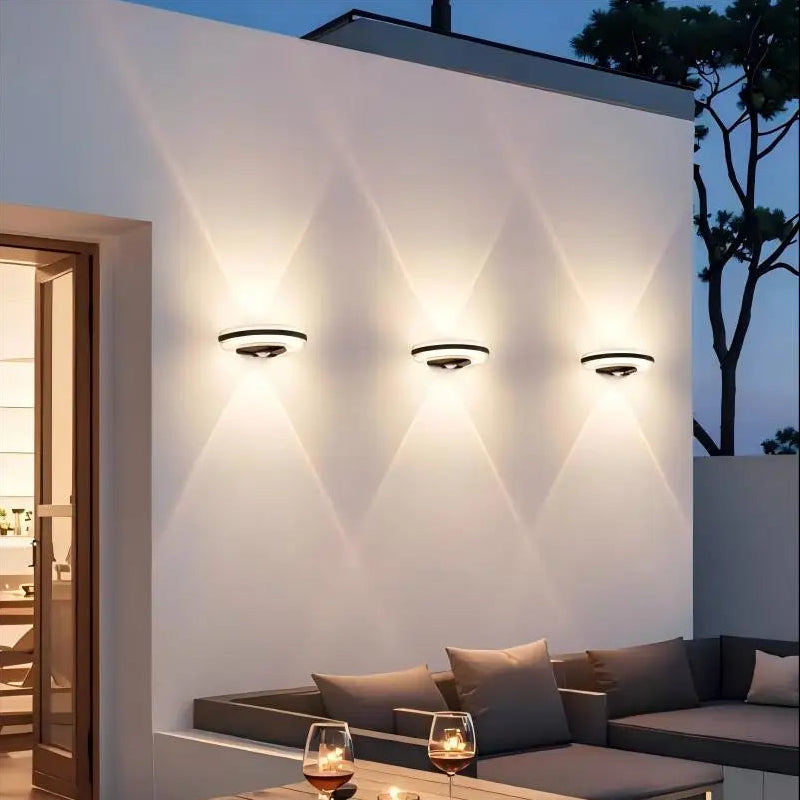 Modern outdoor setting with wall lights, a sofa, and drinks on a table.