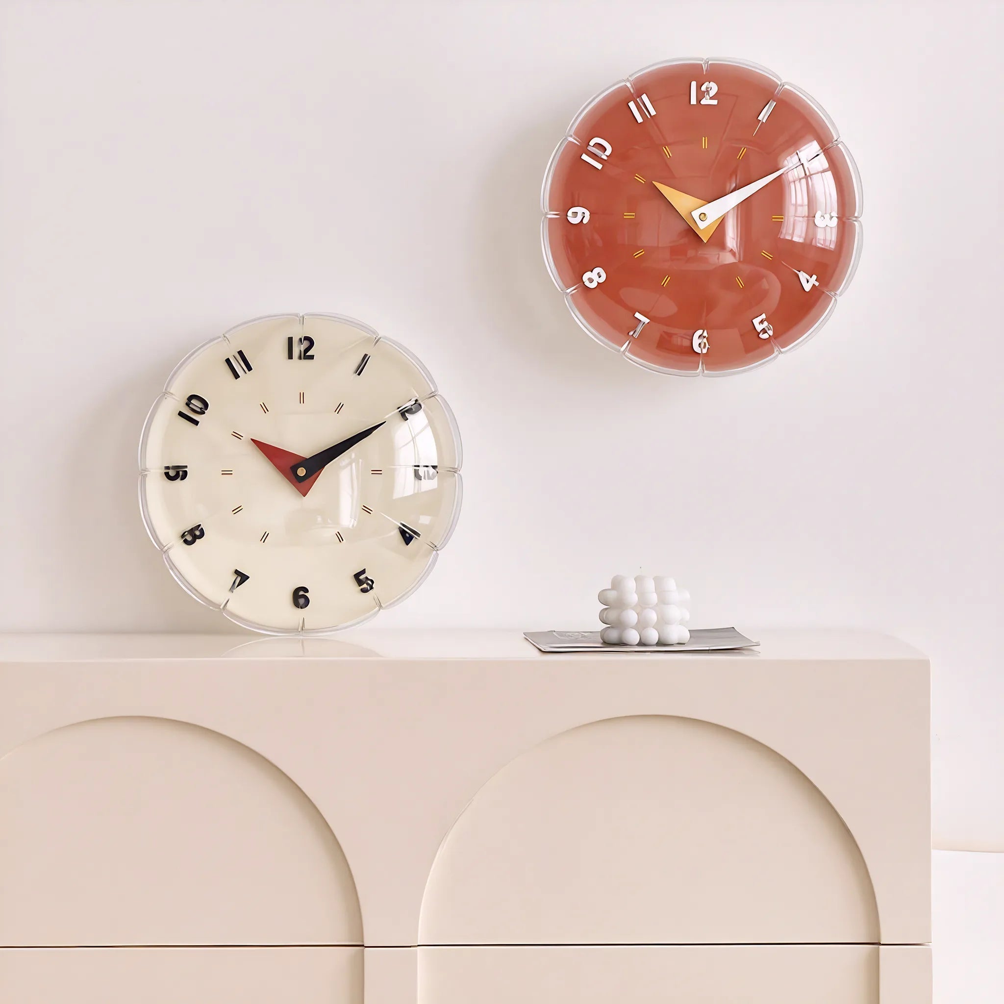 Two wall clocks on a white wall with a decorative object below them.