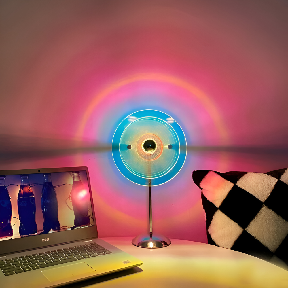 Colorful fan casting a rainbow pattern on a wall next to a laptop and checkered pillow.