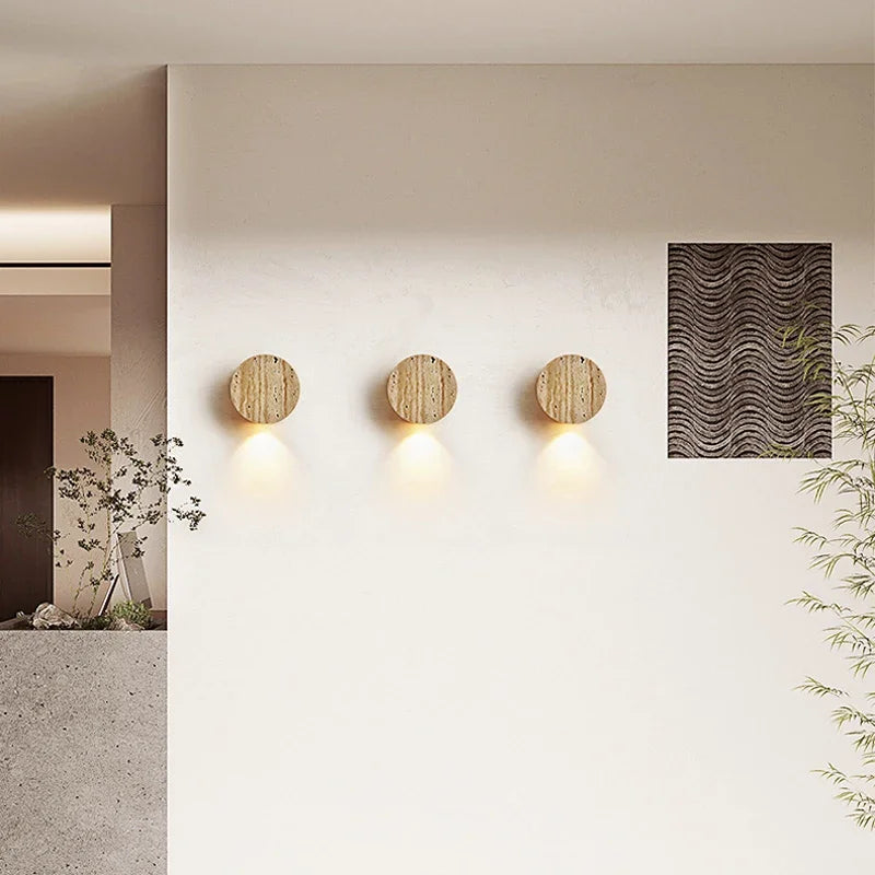 Three round wooden wall lights on a white wall with a textured panel and plants.